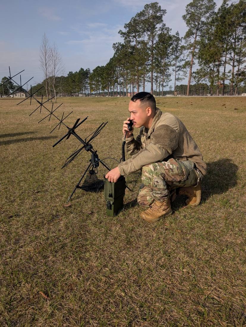 Christian Horton operating a tactical field radio beside a deployed antenna array